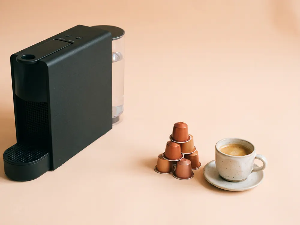 Machine à café noire posée à l'écart de capsules cuivrées et d'une tasse