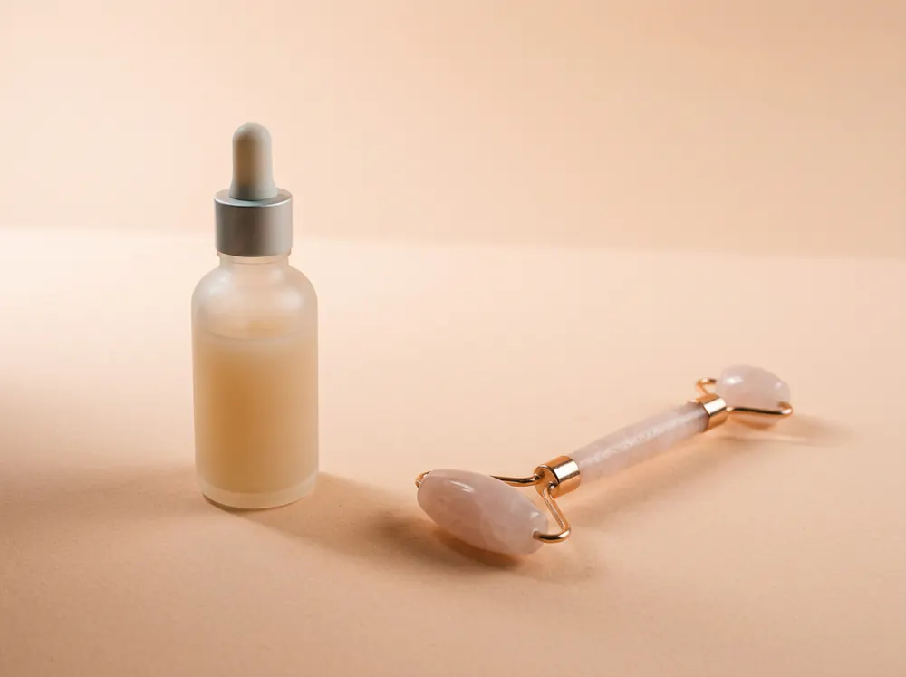 Flacon de sérum en verre dépoli posé à l'écart d'un rouleau en quartz rose